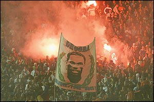 The Marseille fans celebrate their lead with bright red flares and wave a banner of Drogba