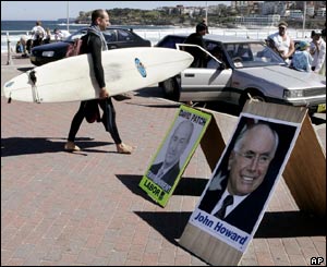 A surfer carries his board past a billboard with a photo of Australian Prime Minister John Howard (r)