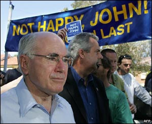 Australian Prime Minister John Howard (l) passes a group of 'Not Happy John' protesters after voting in his Sydney electorate of Bennelong.
