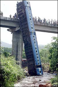 wreckage of train with coaches leaning vertically against bridge over the river valley