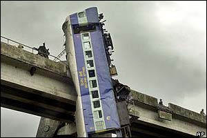 one of the 11 derailed coaches with windows shattered dangles from the bridge parapet