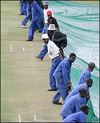 Groundstaff drag covers across the wicket as rain strikes