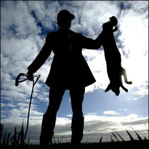 A huntsman holds up a dead fox