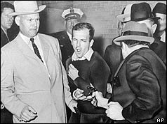 Jack Ruby with gun pointing at Lee Harvey Oswald, flanked by police officers