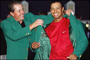 Defending champion Phil Mickelson helps Woods on with the Green Jacket