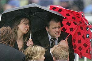 Racegoers hide under an umbrella
