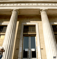 A man with a bag of coins walks past the headquarters of the Bank of Greece
