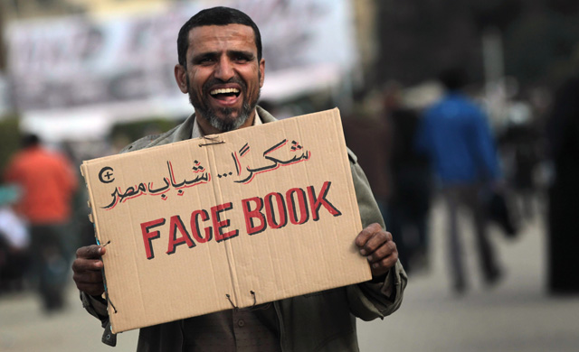 A smiling man holds up a placard, on it is the word 'Facebook' with some Arabic script. (Photo: Getty Images)