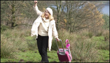 A woman pulling a pink suitcase through a field
