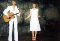 Treflyn Jones mewn 'jumpsuit' gwyn yn canu deuawd