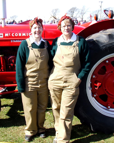 Two women lean on tractors dressed as the womans land army