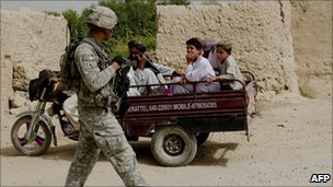 US soldier walks past Afghans on a three-wheeler vehicle in Afghanistan 