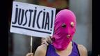Женщина в балаклаве с плакатом "Справедливость!" на испанском языке