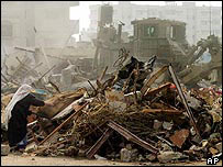 Mulher tenta recolher seus pertences em casa demolida em Rafah