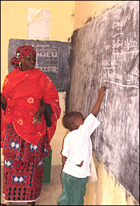 A Nigerian school boy writes on the chalk board in front of his teacher