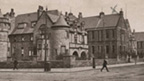 Black and white view of two-storey hospital building featuring a range of pitched-roofed main blocks with turrets. The hospital stands at the crossroads of two wide streets along which run a number of tram tracks.