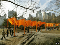 Pedestres passam debaixo de bandeiras, que são sustentadas por arcos de 5,5 metros