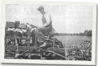 Tomi Jones yn torri gwair hefo 'chassis' pren a hen olwyn beindar.