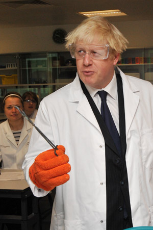 Boris Johnson wearing a big glove, holding some tongs.