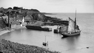 View of Crail with boats in the harbour and white-washed buildings rising up the hill behind.