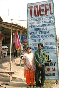 A man and a woman pose in front of a language school's advertisement