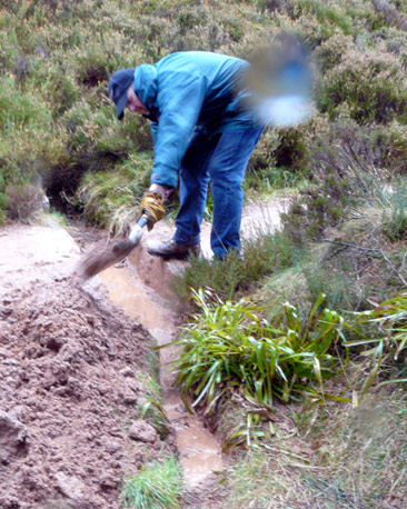 Man digging out channel, in heavy rain