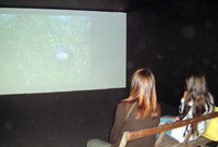 Rhai ymwelwyr â'r Babell Gelf yn edrych ar fideo o waith buddugol Peter Finnemore -enillydd Medal Aur am Gelfydd Gain yn yr Eisteddfod Genedlaethol eleni. 