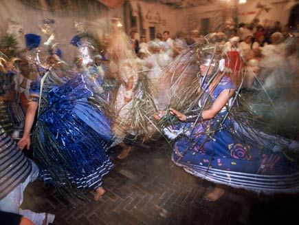 Women dressed in dark blue dresses, with metal hats on their heads. They are all running in one direction.