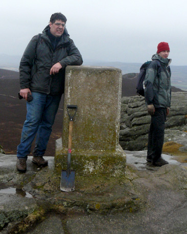 Volunteers beside summit trig point with spade leaning against