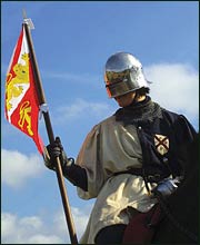 Man dressed as medieval soldier holding a flag.
