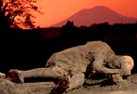 Photograph showing a sunset reddened sky around Vesuvius beyond the poignant cast of a Pompeian's body