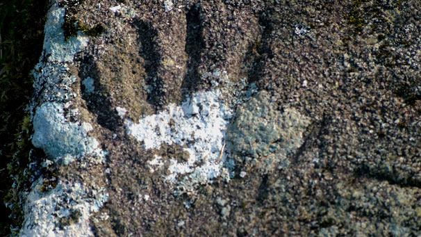 A hand carved into a rock, you can only make it out because shadows have formed in the fingers