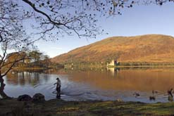 A fly fisherman wades through the still water of Loch Awe, Argyll and Bute, Scotland