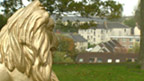 A gold statue of a lion with 20th Century housing behind.
