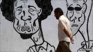 A Libyan man walks past caricatures of Muammar Gaddafi and his son near a courthouse in Benghazi 