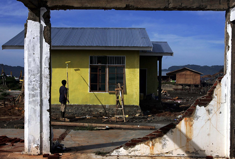 A worker paints a new house beside the ruins of a damaged home in Banda Aceh, Indonesia. REUTERS/Beawiharta
