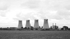 Black and white view across fields to a power station. The view is dominated by four large cooling towers.