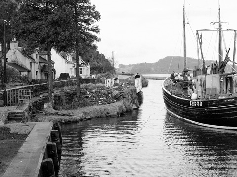 Fishing boat passes small village of Bellanoch as it enters Crinan Canal.