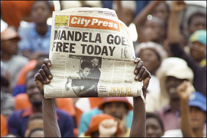 A jubilant man in the crowd holds a newspaper aloft announcing Mandela's release from custody