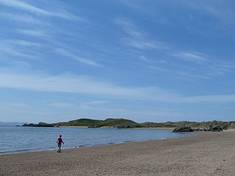 Cerddwr ar y traeth yn Llanddwyn.