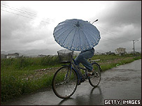 Mulher de bicicleta se protege da chuva na província chinesa de Zhejiang