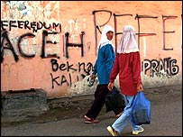 Ženy procházejí v Acehu kolem nápisu za samostatnost regionu