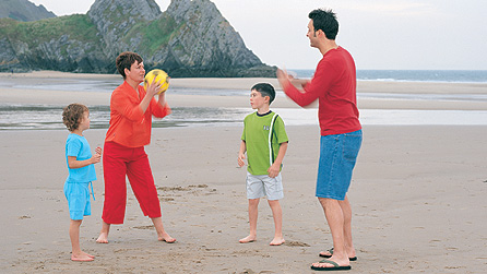 Teulu yn taflu pêl ar y traeth