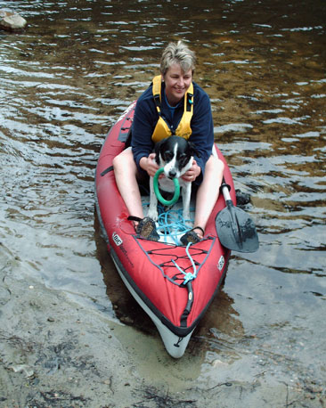 A dog and her owner in an inflatable kayak, on the shore of a loch.