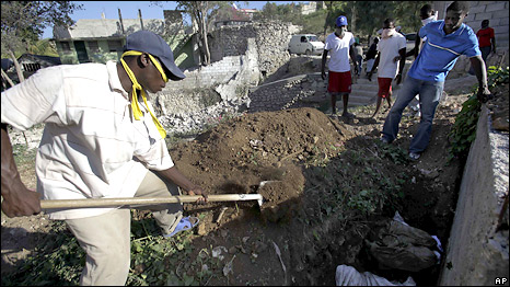 A man watches a cemetery worker cover the remains of his wife and four children in a mass grave in Port-au-Prince, Thursday, 21 January 2010