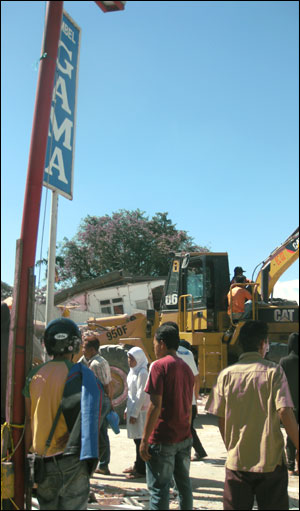 Warga menyaksikan peralatan berat bekerja menyisihkan puing-puing bangunan yang ambru. foto oleh Andreas Nugrohok