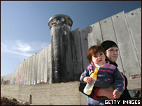 Palestina carrega a filha ao lado de barreira em Belém, na Cisjordânia