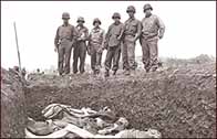 Photograph showing American soldiers gazing down on a mass grave