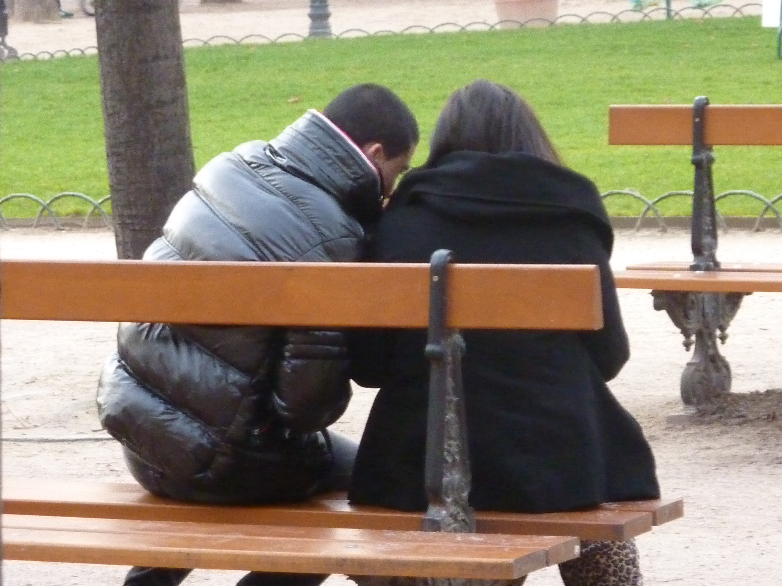 Couple on a bench in a park. Now sitting close together.