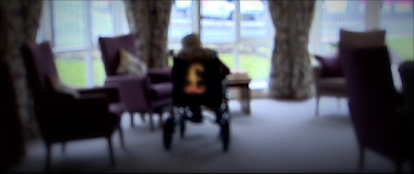 An anonymous elderly resident in a care home with a £ sign on the back of the chair